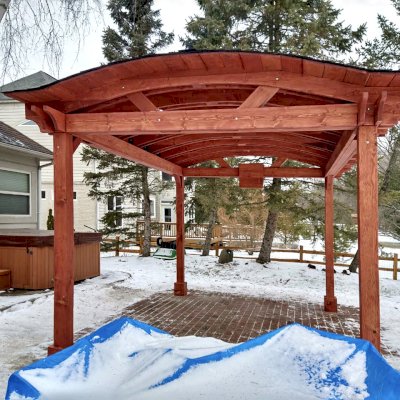 Custom Backyard Pavilion Kit with Extra Supports and Braces on Arches Side (Options: 16' L x 12' Arc W, Douglas-fir, 1 Post Electrical Wiring Trim, 4-Post Anchor Kit for High-Wind, 1 TV Mount Base by Custom Request, No Privacy Panels, No Curtain Rods, 9 ft Post Height, Cherry-Stain Premium Sealant). Photo Courtesy of E. Chen of Ann Arbor, Michigan.